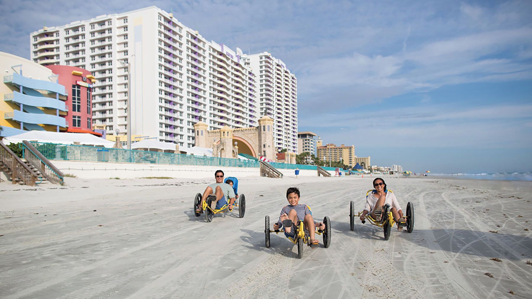 Een zanderig strand met drie mensen in rolstoelen.