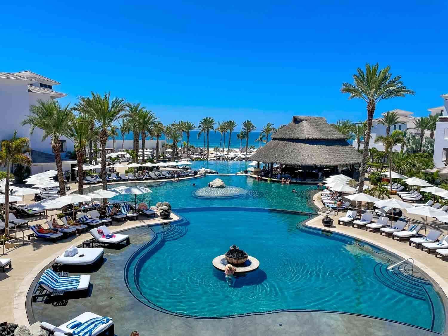 Een resort met meerdere zwembaden, palmbomen en strandparasols.