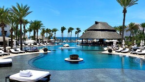 A resort pool with lounge chairs, palm trees, and a thatched-roof structure. - Cabo Azul Hilton Vacation Club 2 Bedroom Ocean View (San José del Cabo)