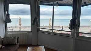 Huone, jossa on suuret ikkunat, joista avautuu näkymä rannalle, sekä puulattia ja patteri.