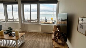 A modern living room with large windows, a wooden floor, a small table with candles, a TV, and a decorative piece on a wooden cabinet. - Captain YOO - The panorama / horizon, fabulous sea view (Fécamp)