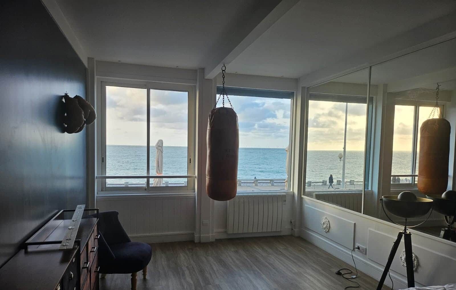 Une pièce dotée de grandes fenêtres donnant sur la mer, d’un sac de frappe et d’une chaise.
