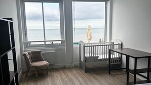 A bedroom with a large window, a bed, a chair, a small table, and a crib. - Captain YOO - The panorama / horizon, fabulous sea view (Fécamp)