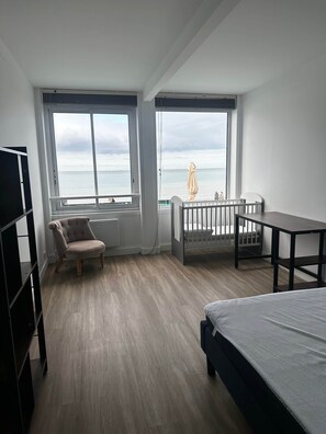 A bedroom with a large window, a bed, a chair, a small table, and a crib.
