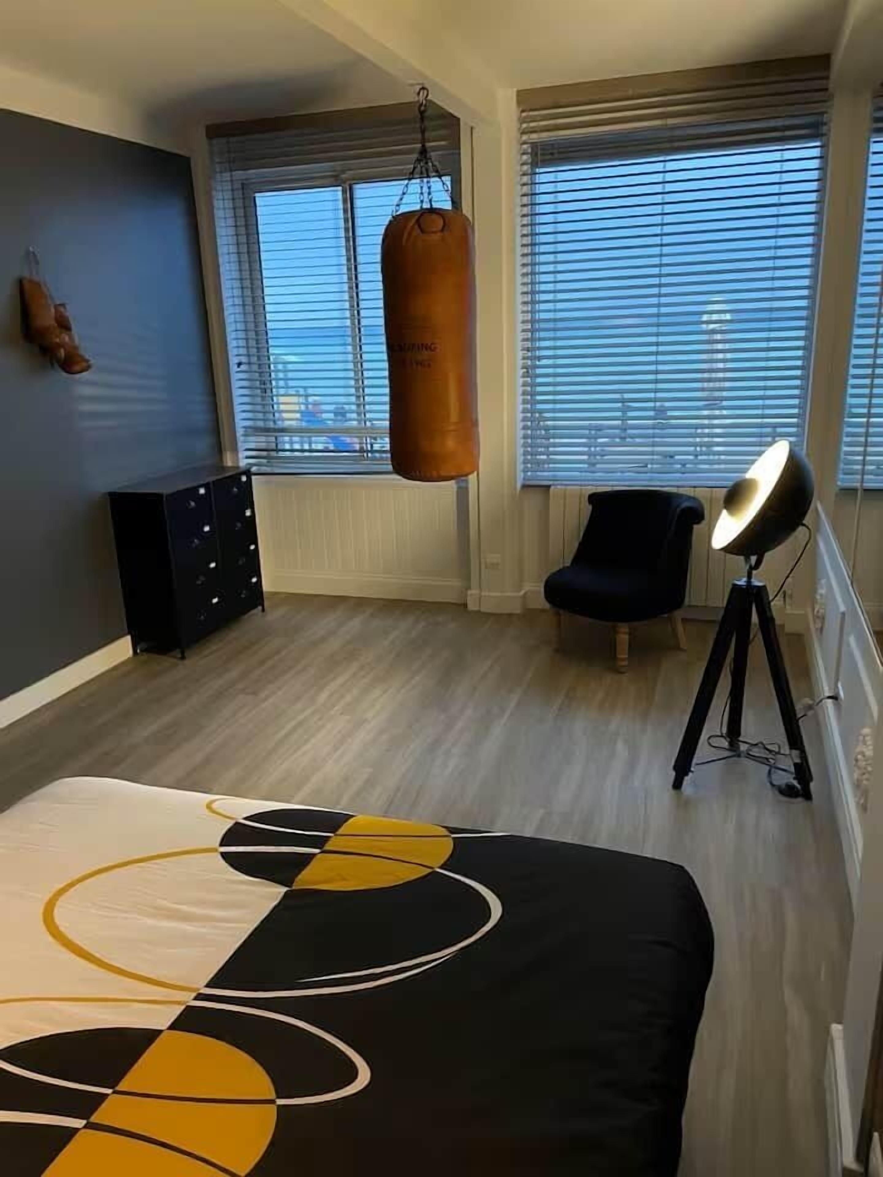 Ein Schlafzimmer mit Bett, einem Boxsack, einem Stuhl, einer Schreibtischlampe und einem Schminktisch.