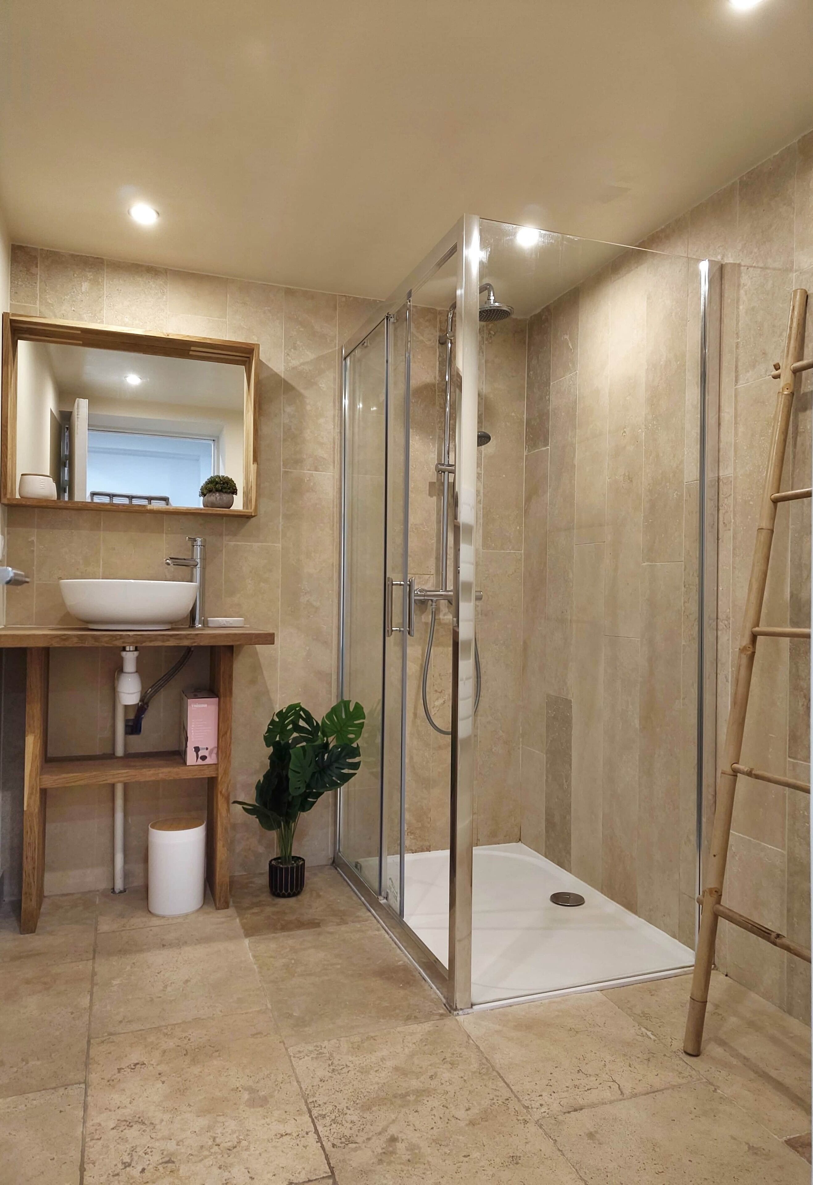 Een moderne badkamer met een douchecabine van glas, een houten wastafelmeubel met een wastafel en een spiegel erboven.