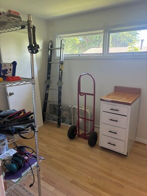 Une pièce comprenant une étagère en métal, un chariot rouge, une armoire blanche et une fenêtre donnant sur des arbres.