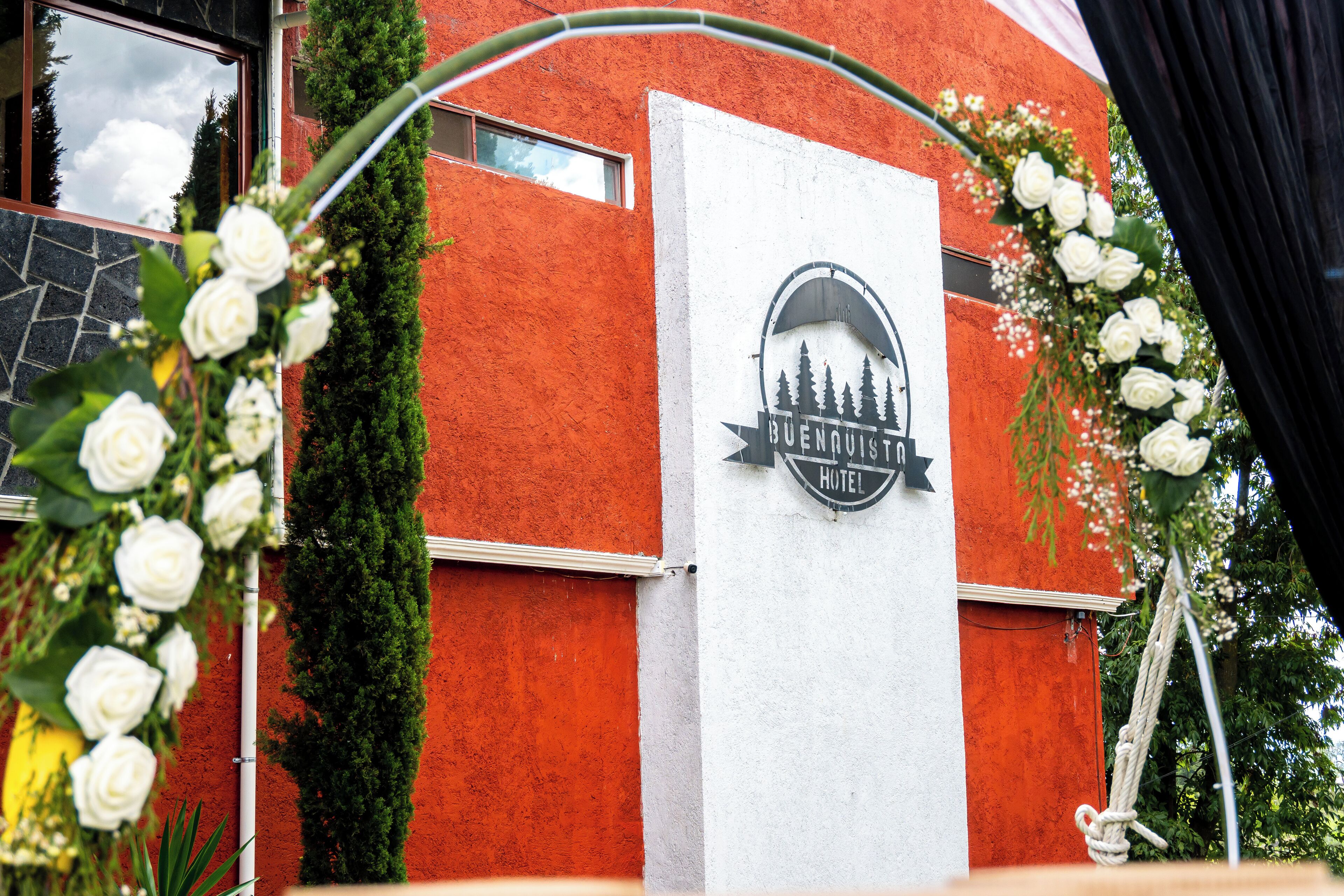 A hotel entrance with a red exterior, a white sign with a logo, and white floral decorations.