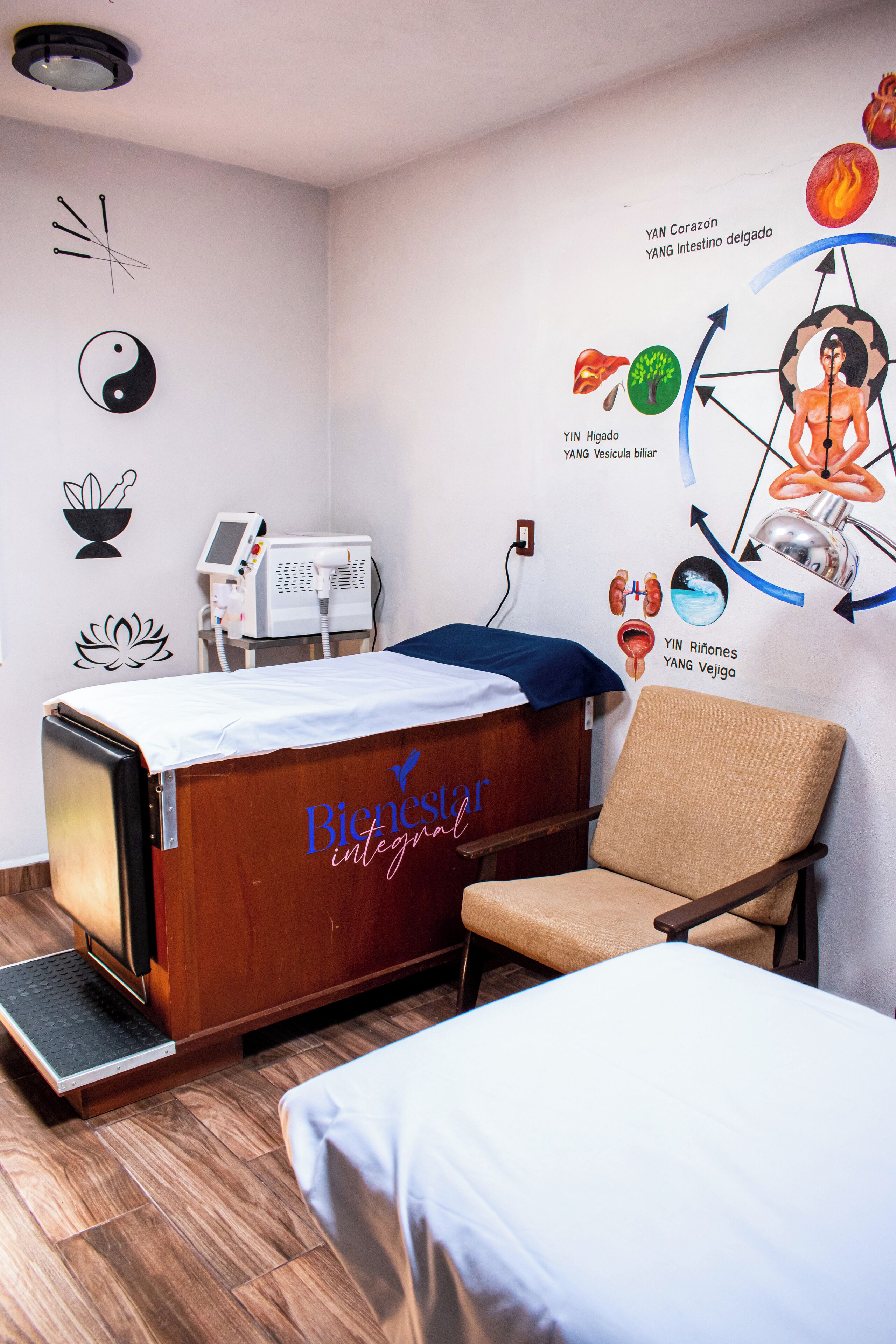 Un consultorio médico con una cama, una silla y una pared decorada con ilustraciones sobre salud.