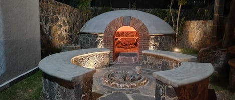 Un four en pierre installé à l’extérieur, doté d’une arche en briques, entouré de sièges en pierre et agrémenté d’un foyer.