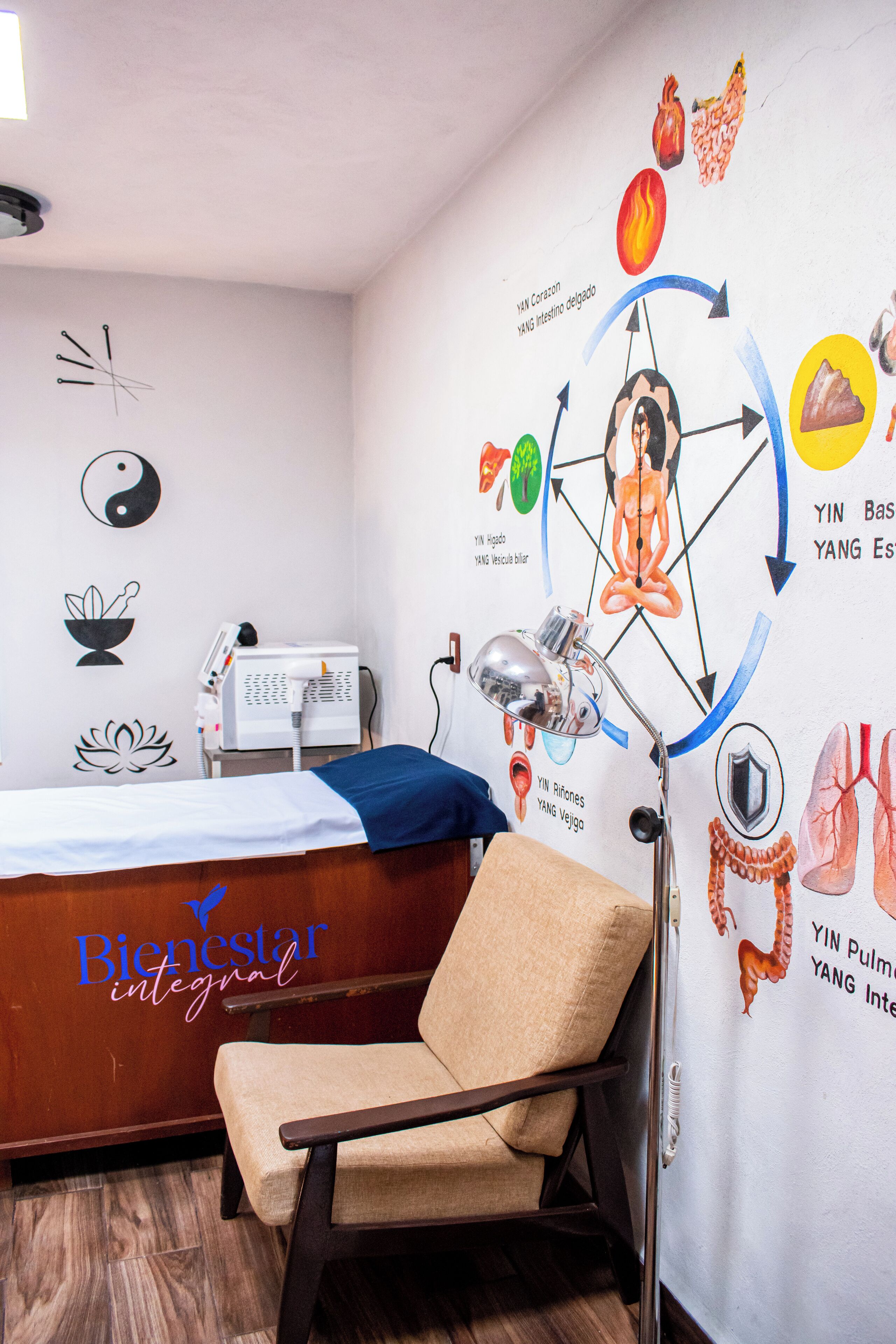 A room with a bed, a massage chair, a wall with a diagram, and a phone on a desk.