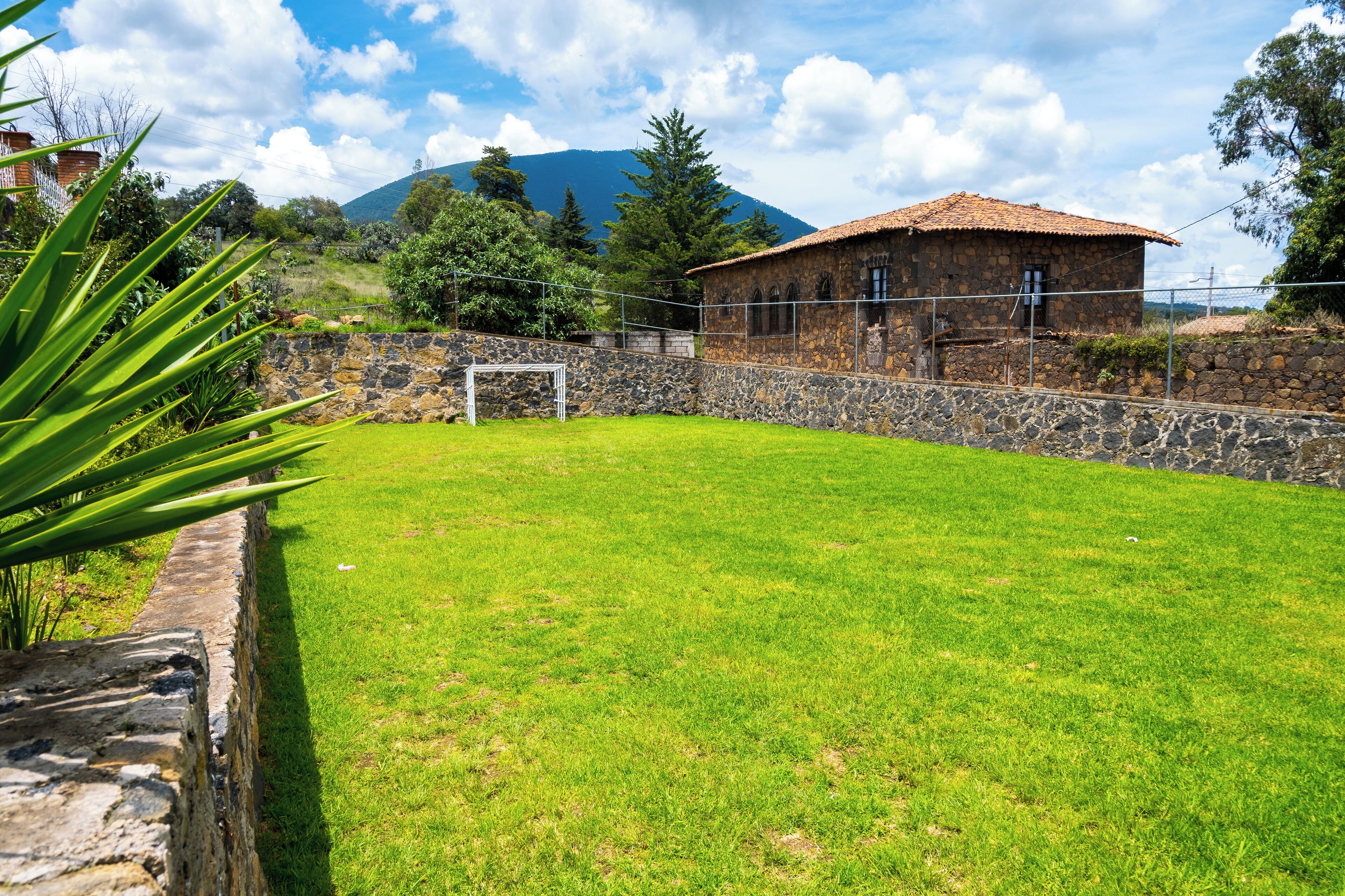 A stone building with a tiled roof, surrounded by a stone wall and a grassy field.
