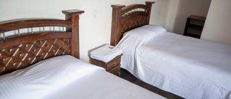 Un dormitorio con dos camas de madera, ropa de cama blanca y una mesita de noche con una lámpara.