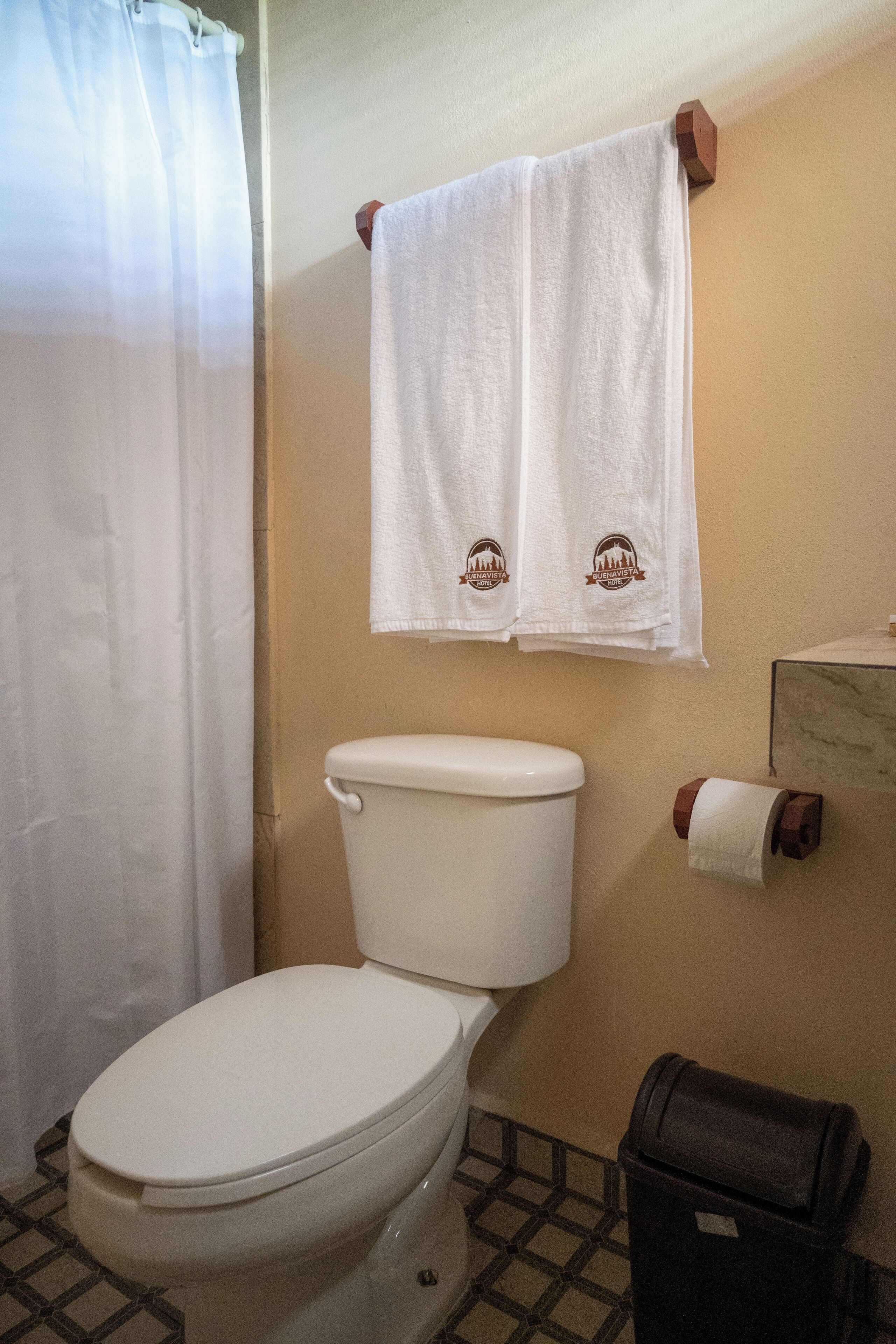 Un baño con inodoro, una toalla colgada en la pared y un cubo de basura.
