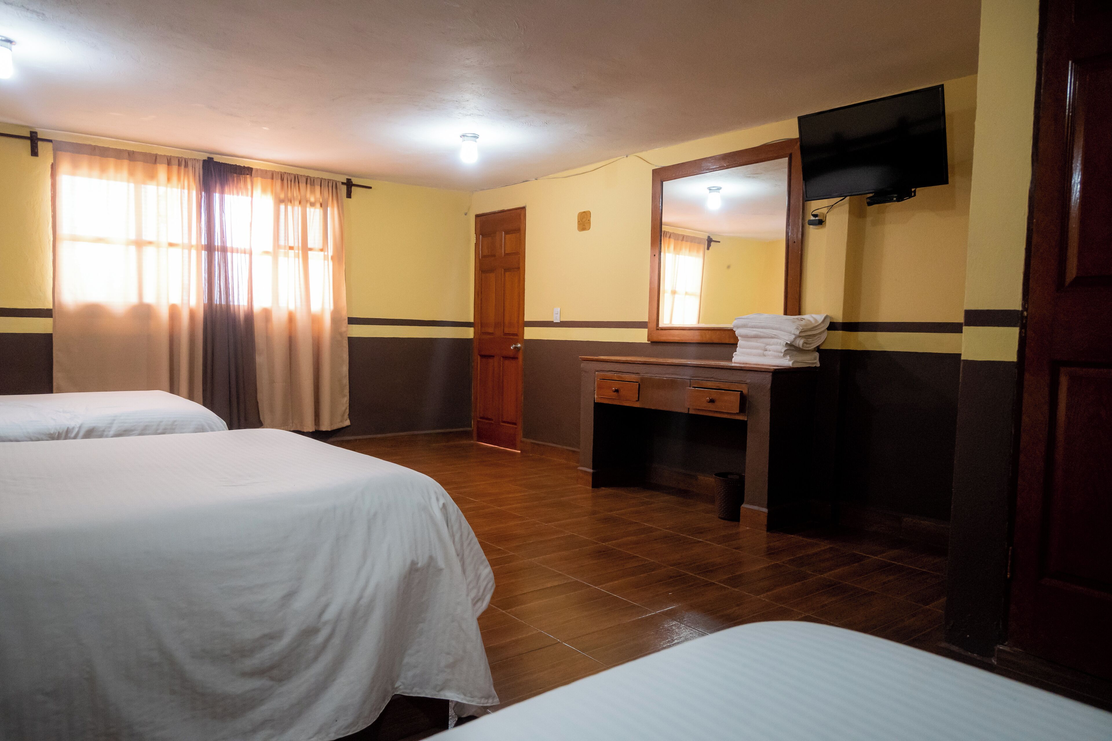 Ein Hotelzimmer mit zwei Betten, einem Holztisch, einem Spiegel und einem Fernseher.