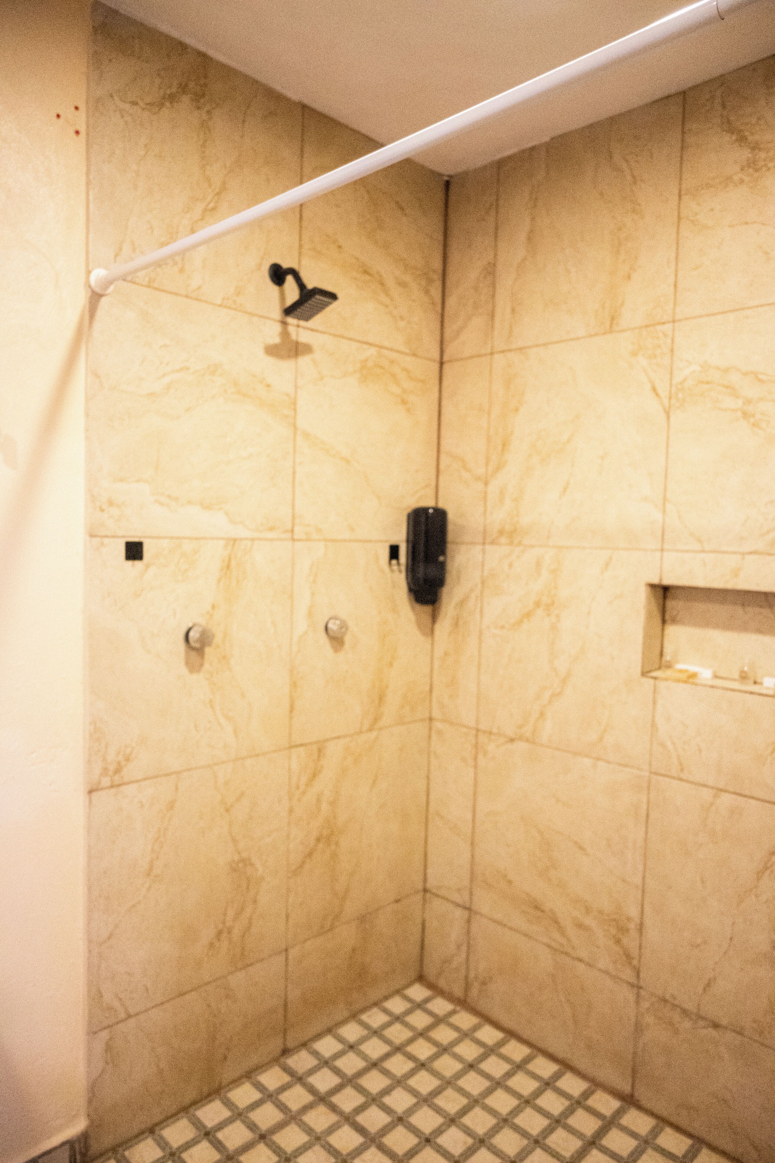 A small, tiled shower area with a handheld showerhead, a towel rack, and a soap dispenser.