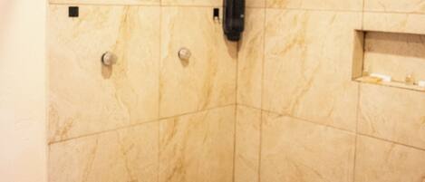 A small, tiled shower area with a handheld showerhead, a towel rack, and a soap dispenser.