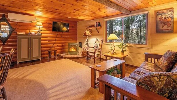 Ein gemütliches Blockhaus-Interieur mit Kamin, Holzmöbeln und einem großen Fenster mit Blick ins Freie.