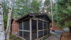 Eine kleine Holzhütte mit Veranda, umgeben von Bäumen und einem Kiesweg.