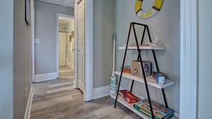 Un pasillo con piso de madera, una puerta blanca y un estante con juegos de mesa.