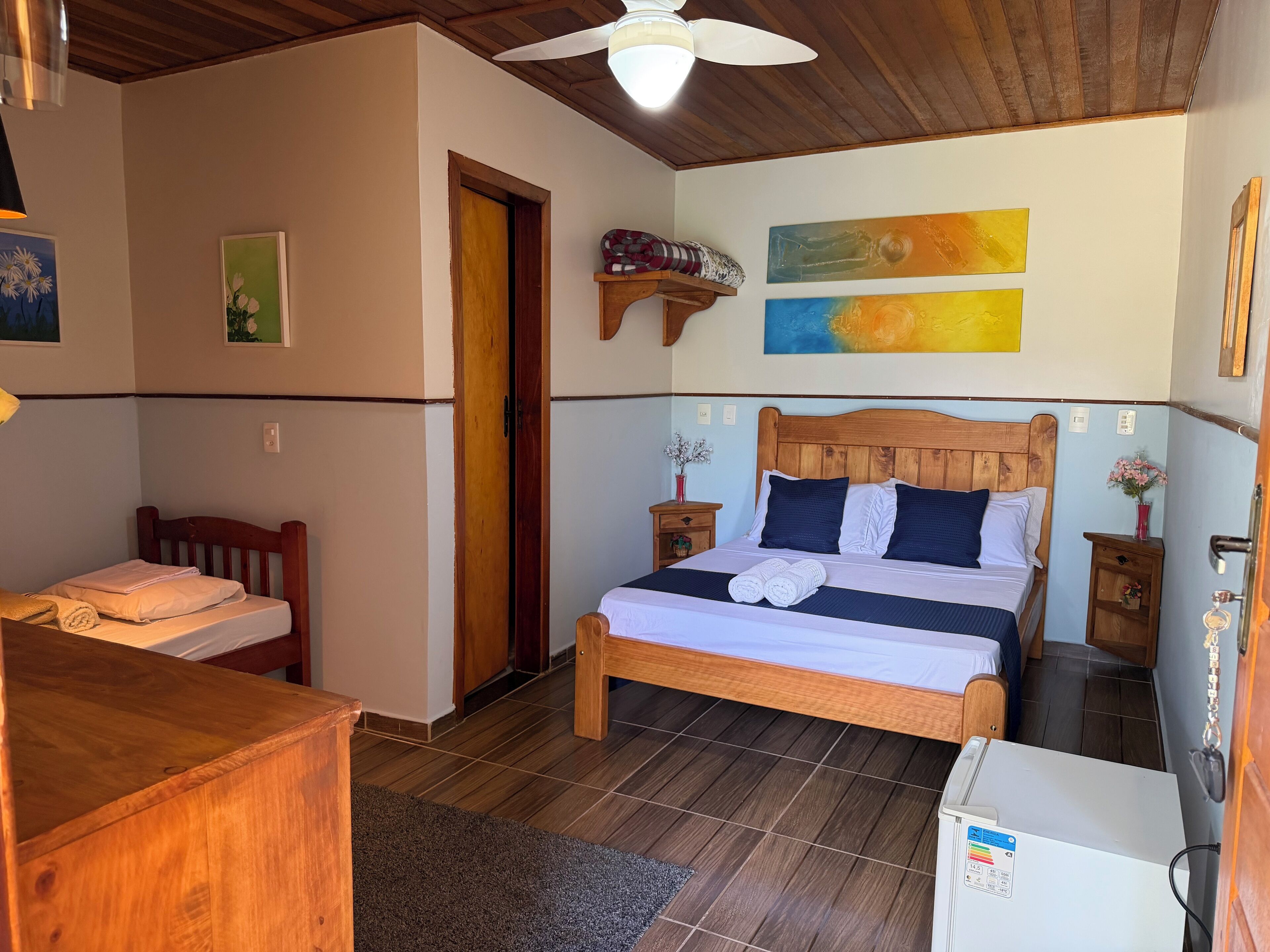 Een slaapkamer met een houten bed, nachtkastje, dressoir en plafondventilator.