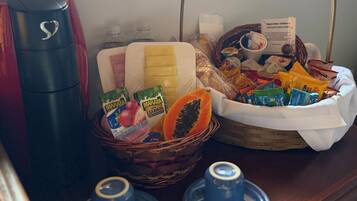 A breakfast setup with a coffee maker, a basket of snacks, and two cups on a wooden table.