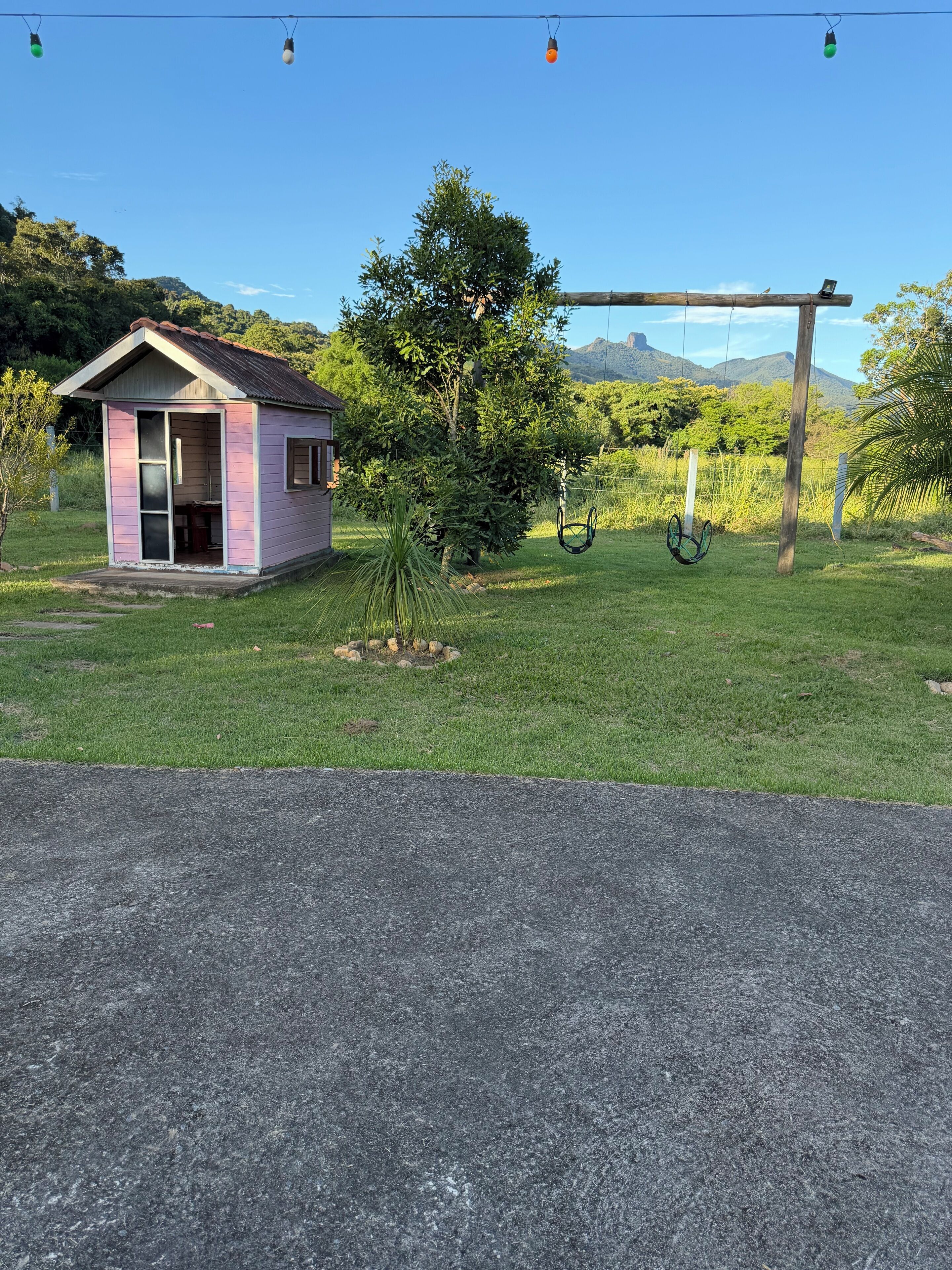 Ein kleines, pinkfarbenes Haus mit Veranda, umgeben von einem Rasen und Bäumen.