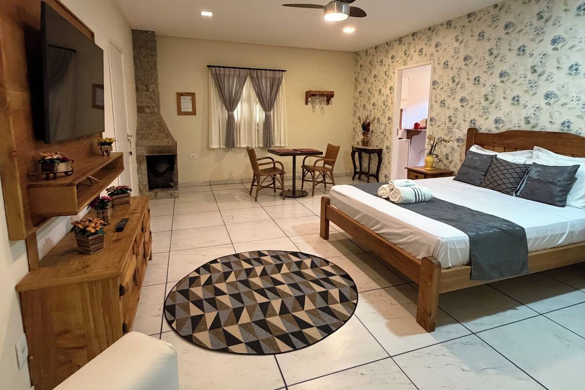 A well-lit room with a bed, a TV, a dining table, and a fireplace.