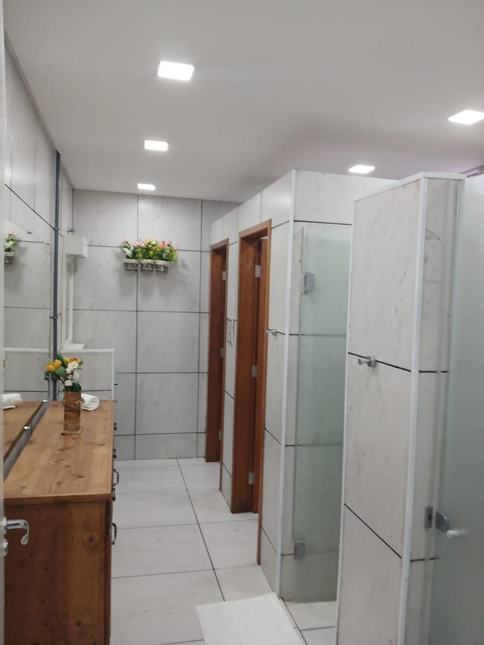 Une salle de bain moderne avec un meuble-lavabo en bois, des murs recouverts de carreaux blancs et une douche à parois de verre.