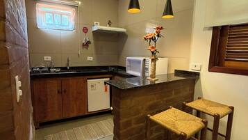 A kitchen with wooden cabinets, a refrigerator, a microwave, and a sink. There are two bar stools and a window with blinds.
