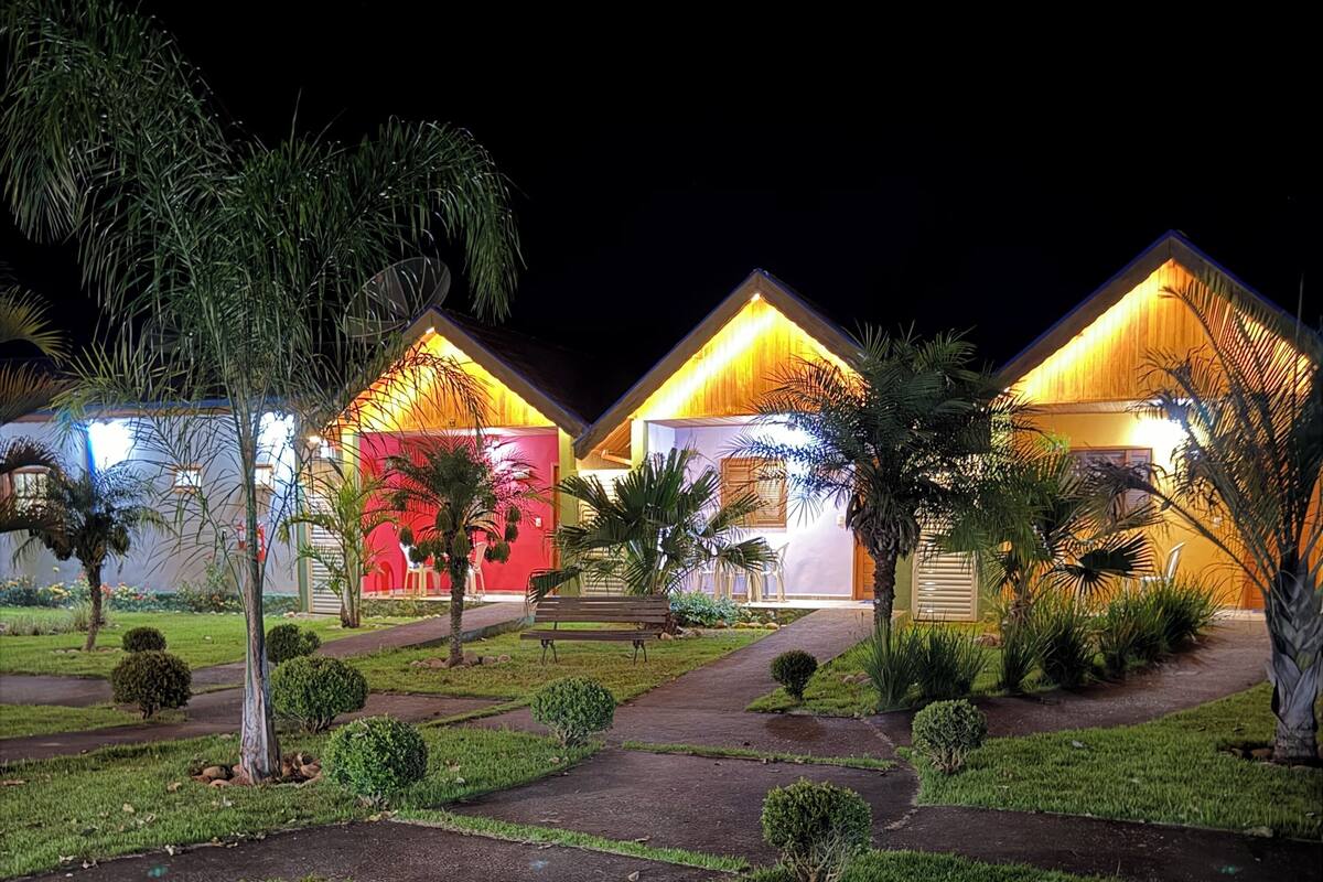 A resort with three brightly lit buildings, a well-maintained garden, and a paved walkway.