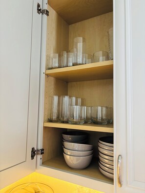 Ein Schrank mit mehreren Einlegebögen, der klare Trinkgläser und gestapelte Schüsseln enthält.