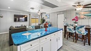 Una cocina moderna con encimera de mármol azul, armarios blancos y una zona de comedor con sillas y mesa de madera.