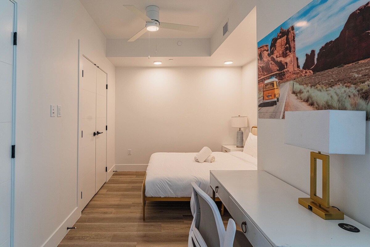 A hotel room with a bed, desk, and a painting of a desert landscape.