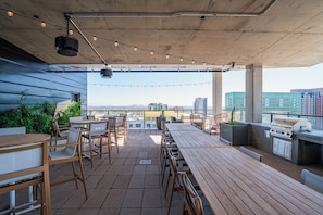 An outdoor patio with wooden tables and chairs, a grill, and potted plants. - Saiya (Phoenix)