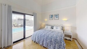 Une chambre à coucher comprenant un lit, une table de chevet, deux lampes fixées au mur, une porte-fenêtre coulissante et deux tableaux encadrés accrochés au mur.