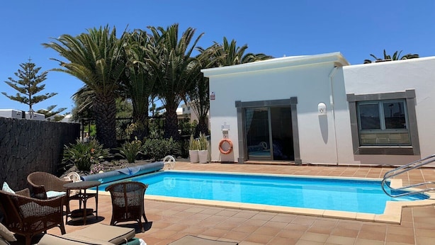 Une piscine avec des chaises longues et un petit bâtiment doté d’une porte et de fenêtres.