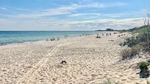 Uma praia arenosa com pessoas, céu claro e mar calmo.