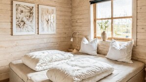 Quarto de madeira com uma cama, duas imagens penduradas na parede, uma luminária de cabeceira e uma janela com vista.