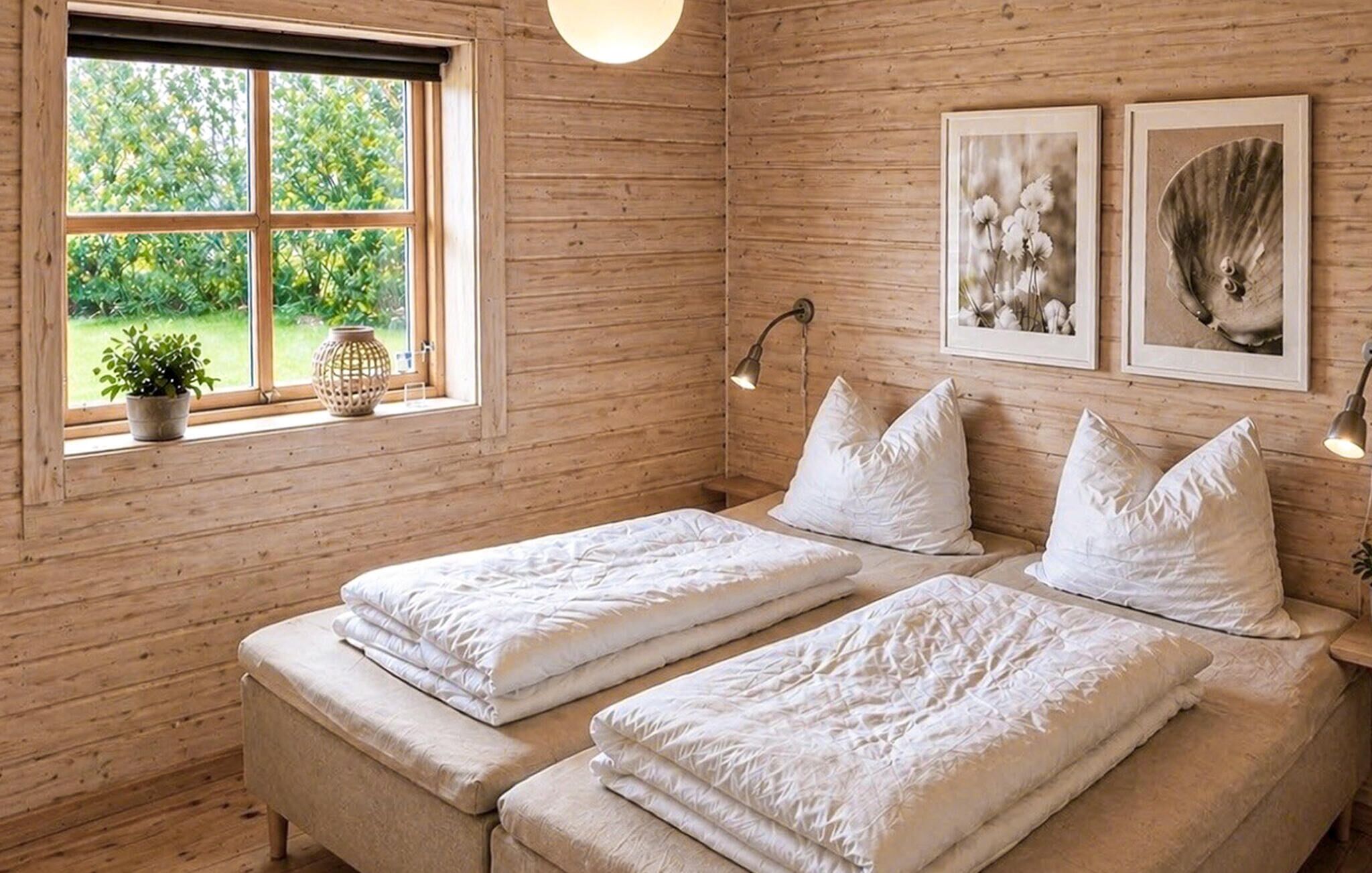 A wooden room with two beds, a window with plants, and two wall-mounted lamps.