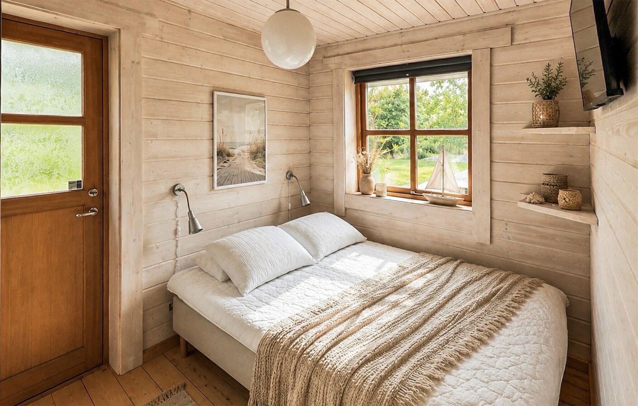 Une pièce en bois avec un lit, une fenêtre donnant sur un paysage agréable, une porte et une étagère ornée d’objets décoratifs.
