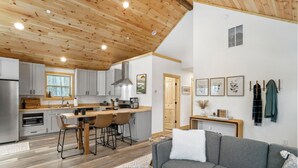 Una cocina moderna con armarios de madera, un comedor con una mesa y sillas, y un sofá gris en la sala de estar.