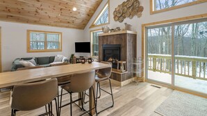 Un salón amplio con techo de madera, ventanas grandes, chimenea y una mesa de comedor con sillas.