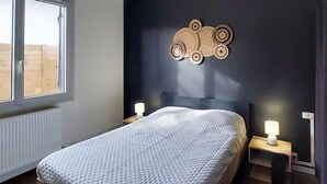 Et soveværelse med en seng, to sengeborde med lamper, et vindue og en dekorativ genstand på væggen.