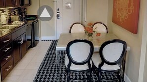 Un comedor con una mesa, sillas, una araña de techo y un tapete de estampado pata de gallo.