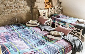 Una stanza con due letti, ognuno con una coperta e cuscini a quadri colorati. Sullo sfondo, una parete in pietra e un poggiatesta in metallo bianco.