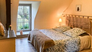 Et soveværelse med en seng, et natbord, en lampe og et vindue med udsigt til grønne omgivelser.