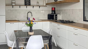 A modern kitchen with white cabinets, a black countertop, a gas stove, a microwave, and a vase with flowers on the table. - 3 bedroom gorgeous home in Parigné (Parigné)