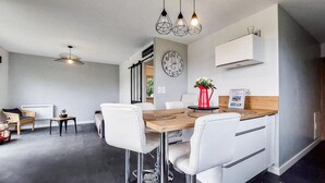 Cozinha moderna com área de refeições, apresentando uma mesa de madeira, cadeiras brancas e iluminação pendente.