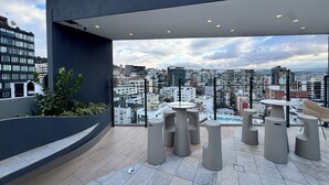 A rooftop terrace with modern tables and chairs, a view of the cityscape, and a mix of greenery and architectural elements. - Deluxe green suite/ La Carolina (Quito)